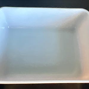 May include: A rectangular, white baking dish with rounded corners and two small handles on the sides. The dish has a smooth, glossy surface and is empty. The overall shape is a classic design for baking and serving.