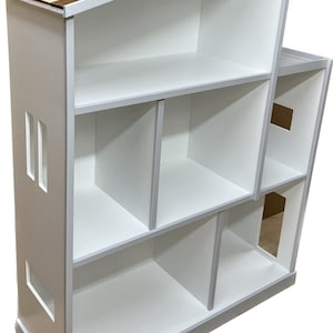 May include: White wooden dollhouse with a brown wood shingle roof. The dollhouse has multiple rooms and windows.