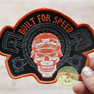 May include: Orange and black embroidered patch with a skull wearing a helmet and the text "Built for Speed".
