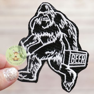 May include: Black and white embroidered patch of a Bigfoot carrying a box that says "BEER" on it.