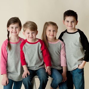 Peut inclure: Quatre enfants portant des chemises de baseball grises et color&eacute;es avec des manches contrast&eacute;es. Les chemises ont une bordure noire, rouge, rose et noire. Les enfants sont debout en rang, regardant la cam&eacute;ra et souriant.