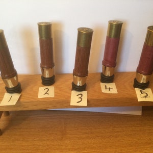 Könnte beinhalten: Fünf Flaschenverschlüsse aus Holz mit Messingköpfen, nummeriert von 1 bis 5, auf einem Holzständer ausgestellt.