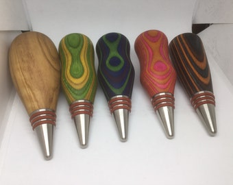 May include: Five wooden bottle stoppers with different wood grain patterns and colors. The stoppers have a silver metal base and a brown rubber ring.