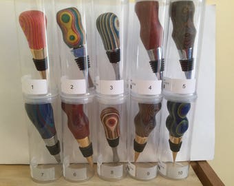 May include: Ten colorful wooden bottle stoppers in clear plastic containers. Each stopper is numbered 1 through 10. The stoppers are made of different types of wood and have unique patterns.