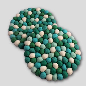 May include: Two round felt coasters in shades of green, white, and blue. The coasters are made of small, round felt balls.