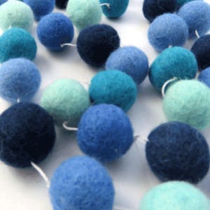 May include: A garland of felt balls in shades of blue and teal. The balls are strung together with white thread and are perfect for adding a touch of color to any room.