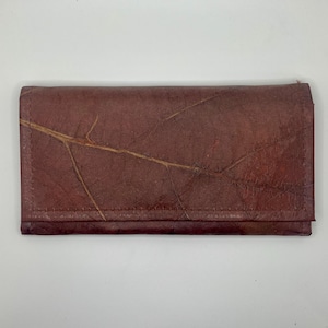 May include: A brown leather wallet with a unique leaf pattern. The wallet is closed and has a stitched seam around the edges.