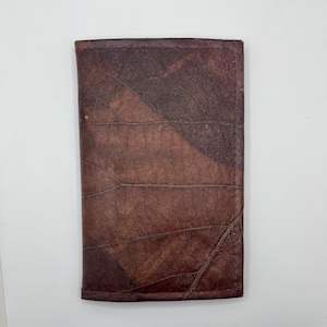 May include: A brown leather wallet with a unique leaf pattern. The wallet has a stitched edge and a rectangular shape.