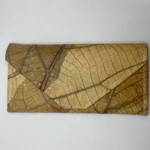 May include: A brown leather wallet made from pressed leaves. The wallet has a unique, natural pattern and is stitched together with a light brown thread.