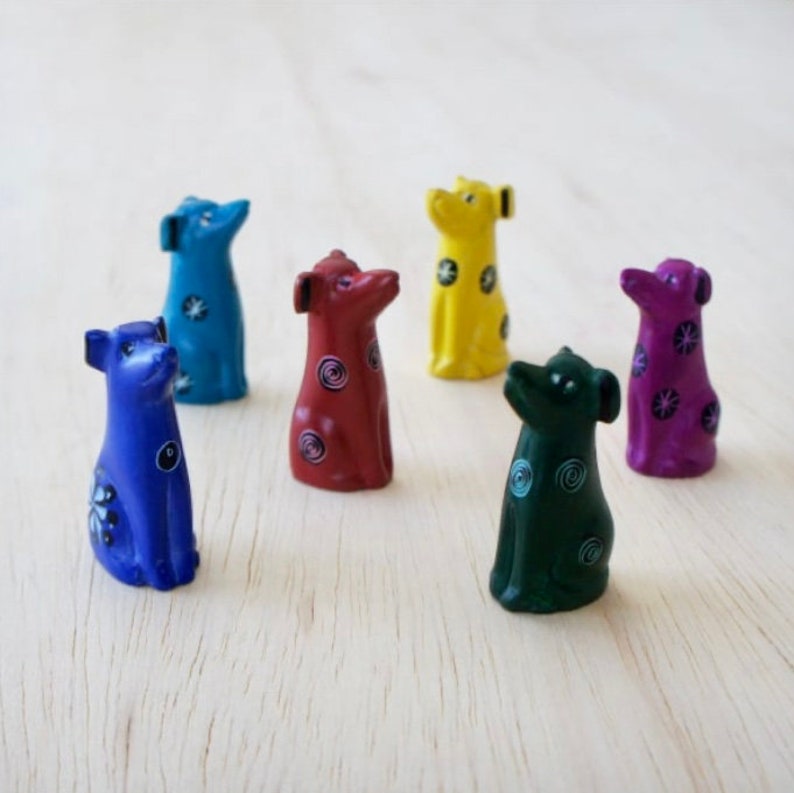 May include: Six small, hand-painted wooden dog figurines in various colors, including blue, red, yellow, green, and purple. Each figurine has a unique design with circles and swirls.