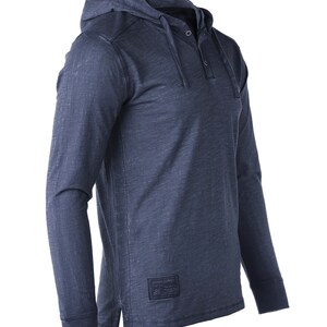 May include: A dark blue long-sleeved hooded shirt with a single button closure at the neck. The shirt has a distressed look and a small logo patch on the bottom right side that says "Ocean Supply Co."
