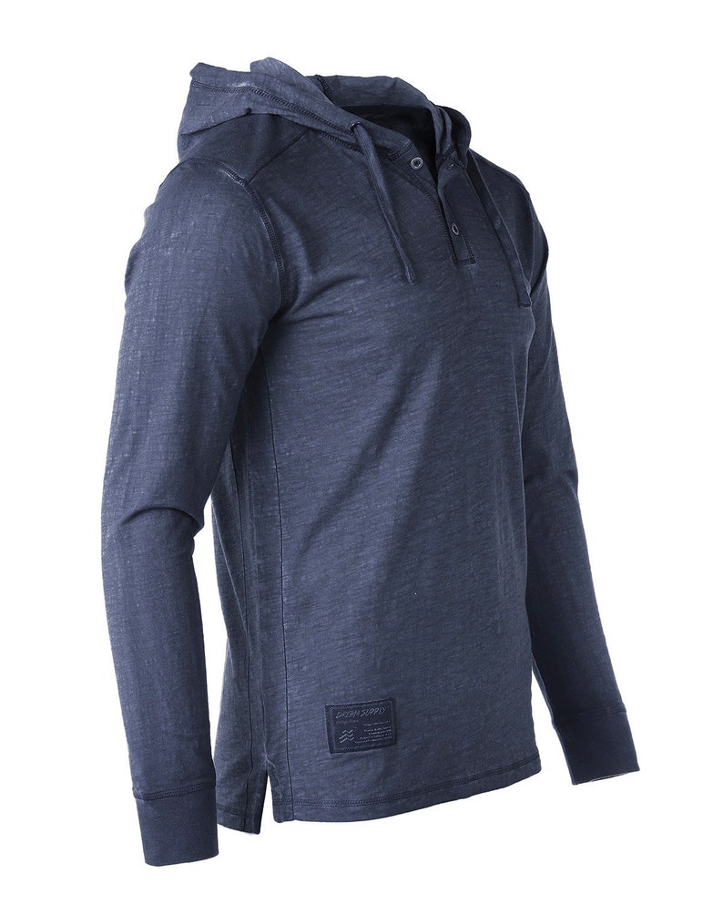 May include: A dark blue long-sleeved hooded shirt with a single button closure at the neck. The shirt has a distressed look and a small logo patch on the bottom right side that says "Ocean Supply Co."