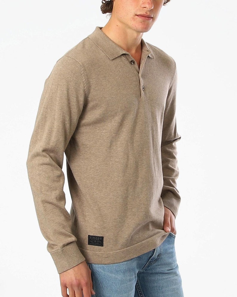 May include: A long-sleeved, light brown knitted polo shirt with a button-up collar and a small black patch label that reads "ZINEGO" on the left side of the shirt.