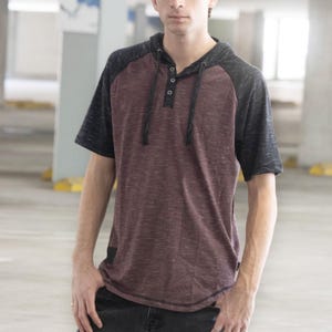 May include: A short-sleeved hooded shirt with a burgundy body and black sleeves. The shirt has a three-button placket and a drawstring hood. The sleeves are a contrasting dark gray color. The shirt is made of a soft, textured material.