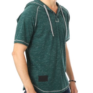 May include: A green short-sleeved hooded shirt with a button placket and a small black patch on the side. The shirt has a grey drawstring hood and grey stitching.