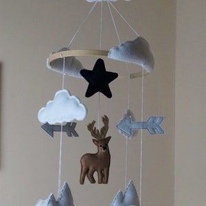 May include: A handmade baby mobile featuring felt clouds, a black star, gray arrows, a brown deer, polar bears, and gray mountains. The mobile is suspended from a wooden hoop with white string.