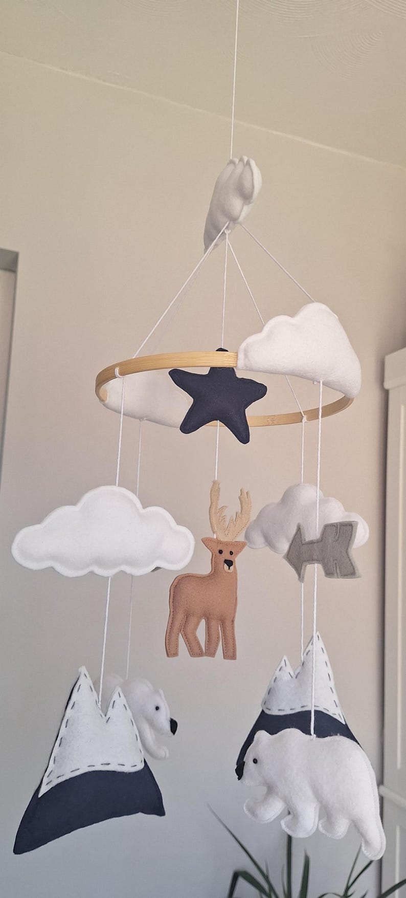 May include: A handmade baby mobile featuring a wooden hoop with felt clouds, a navy star, a brown deer, gray arrow, white polar bears, and navy and white mountains. The mobile is suspended by white strings.
