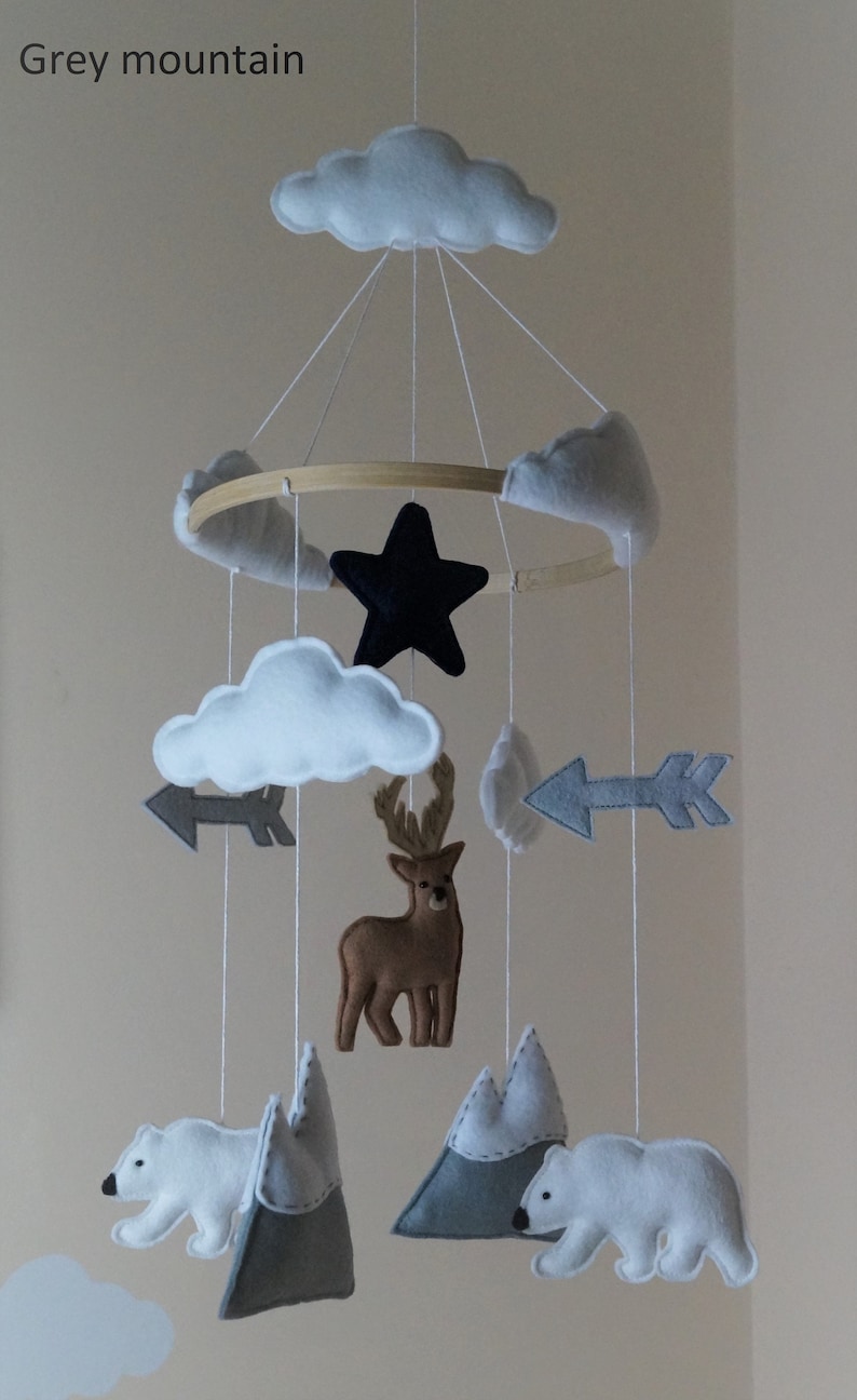 May include: A baby mobile featuring felt clouds, arrows, a black star, a deer, polar bears, and mountains. The mobile is suspended from a wooden ring. The text "Grey mountain" is in the upper left corner.