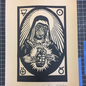 Può includere: Stampa linoleografica in bianco e nero su carta beige. L'opera raffigura una figura simile a una scimmia che tiene una granata, circondata da un'aureola e simboli. La stampa è firmata a matita. Lo sfondo è una griglia.