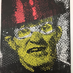 以下が含まれることがあります： 黒い背景に、黄色と白のハーフトーンの点で描かれた顔が特徴的な抽象的なアートプリント。上部には赤いハーフトーンの点があります。作品は右下に署名されています。