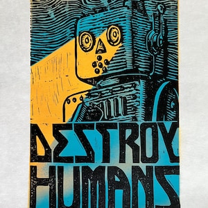 May include: A black and blue linocut print of a robot with the text "DESTROY HUMANS" in black and blue. The robot has a yellow face with black eyes and a black mouth.