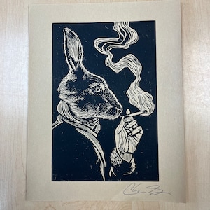 May include: Black and white linocut print of a rabbit smoking a cigarette with smoke rising from the cigarette. The rabbit is wearing a scarf and has a serious expression on its face.