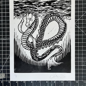 Può includere: Stampa linoleografica in bianco e nero raffigurante un serpente marino. L'opera d'arte raffigura una creatura serpentina con un corpo strutturato e dettagliato, su uno sfondo di onde stilizzate e linee verticali. Firmato dall'artista.