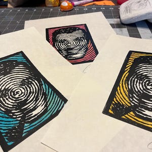 以下が含まれることがあります： 黒と白の渦巻き模様のプリントが3枚。それぞれ背景の色が異なります。ターコイズ、イエロー、ピンクです。