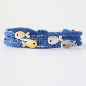 May include: Blue braided bracelet featuring silver and gold fish charms. The bracelet is made of multiple strands of blue cord, and the fish charms are evenly spaced around the bracelet.