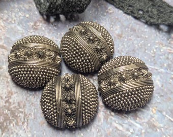 May include: Four antique silver-colored buttons with intricate detailing. Each button features a textured, beaded surface, accented with star-shaped embellishments and vertical bands. A dark gray lace ribbon is in the background.