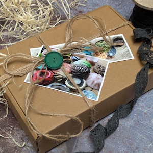 May include: A brown cardboard box tied with twine and a green button. The box is decorated with a small photograph of colorful candies. A spool of black lace and straw-like material are also visible.