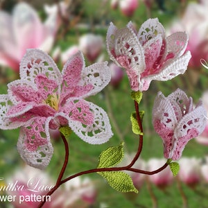 May include: Crocheted magnolia flowers in shades of pink and white, with green leaves and brown stems. The flowers are intricately detailed with a lace-like pattern. The image includes the text "Magnolia flower" and "Tanitka Lace flower pattern".