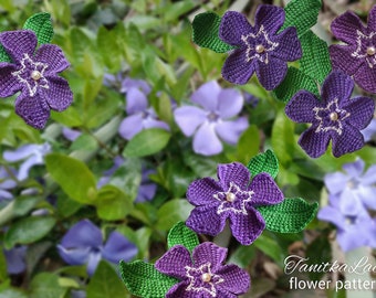 Puede incluir: Cinco flores moradas de ganchillo con hojas verdes y una pequeña perla blanca en el centro de cada flor. Las flores presentan detalles bordados en blanco alrededor del centro. El texto TanitkaLace flower pattern es visible abajo a la derecha.