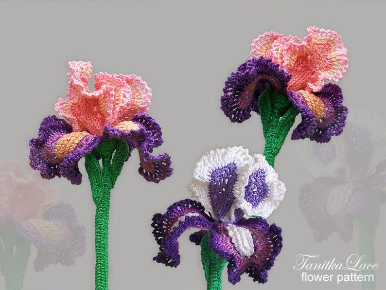 May include: Three handmade crochet iris flowers in shades of pink, purple, and white. The flowers have green stems and are set against a gray background. The text "Tanitka Lace flower pattern" is visible in the bottom right corner.