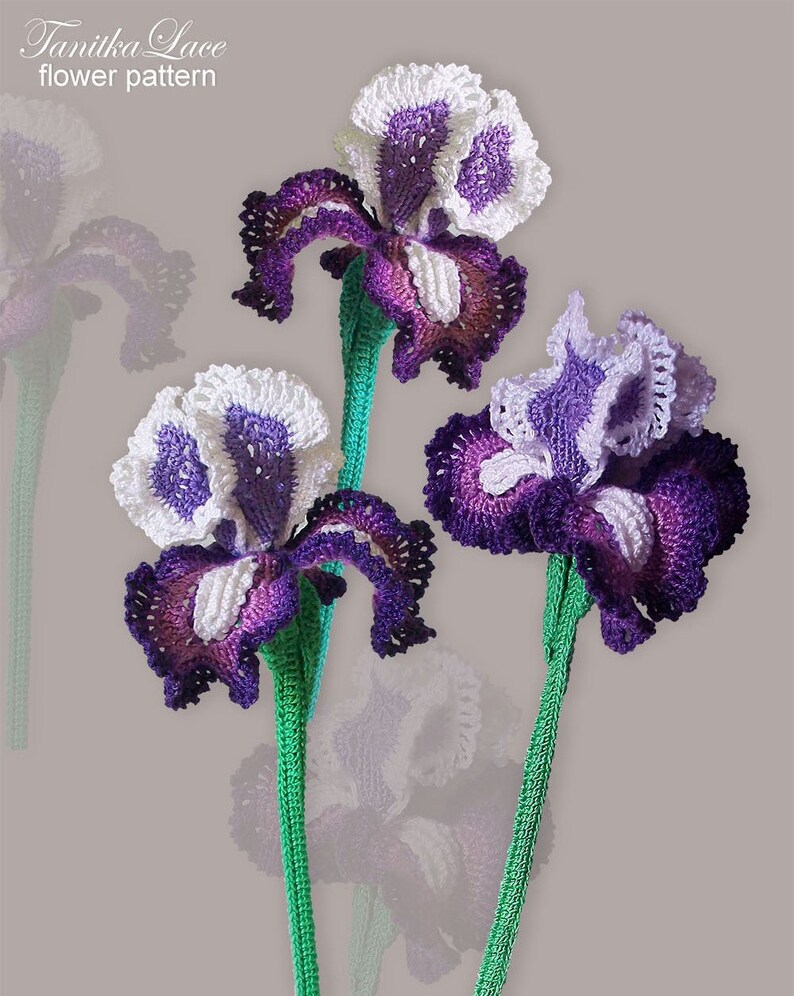 May include: Three handmade crochet iris flowers in shades of purple, white, and brown, with green stems. The flowers have intricate petal details and are set against a neutral background. The text "Tanitka Lace flower pattern" is in the upper left corner.