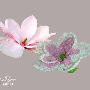 May include: Two flower patterns. One is a light pink magnolia with a yellow and pink center. The other is a crocheted flower with white, pink, and green accents. The text "Tanitka Lace flower pattern" is at the bottom.