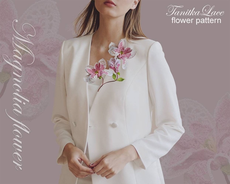 May include: A white blazer with a delicate, handcrafted magnolia flower brooch. The brooch features pink and white lace petals with green stems. The text "Magnolia Flower" and "Tanitka Lace flower pattern" are visible.