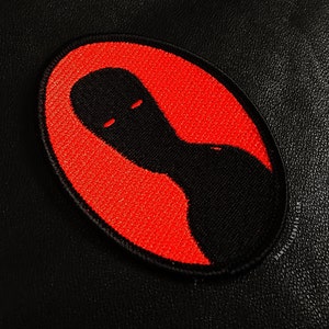 Könnte beinhalten: Ein gestickter schwarzer und roter Aufnäher mit einer Silhouette einer Person auf rotem Hintergrund. Der Aufnäher hat einen gestickten Rand.