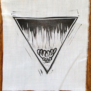 May include: Black and white print of a triangle with a design inside on a white fabric background.