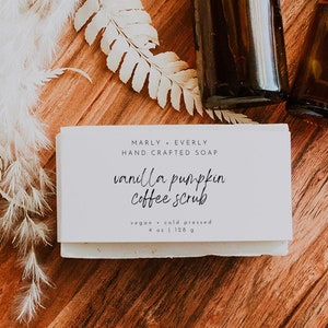 May include: A white bar of soap with the text "Marly + Everly Hand Crafted Soap" and "small batch pumpkin coffee scrub" on a wooden surface with two brown glass bottles.
