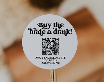 May include: A white round sticker with black text that reads "Buy the bride a drink!" and a black and white QR code. The text below the QR code reads "AVA'S BACHELORETTE 10/27/20xx Asheville, NC".