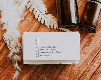 May include: A white bar of soap with the text "Cold Pressed Vegan Hand Crafted Soap Rosemary & clove 1.00 oz | 148 g" on a wooden surface with two amber glass bottles with droppers.