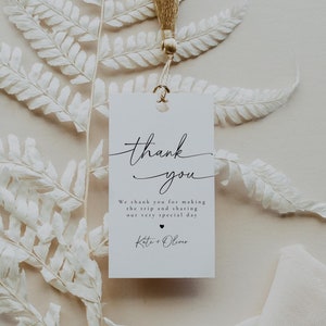 May include: A white tag with the words "thank you" in elegant script, suspended from a gold tassel. The tag includes a message and names, set against a backdrop of a white fern and cream-coloured ribbon.