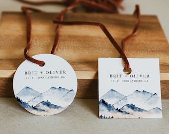 May include: Two wedding favor tags with a watercolor mountain design. The tags are tied with brown string. The text on the tags reads "BRIT + OLIVER 11.11.20XX | ATHENS, GA".