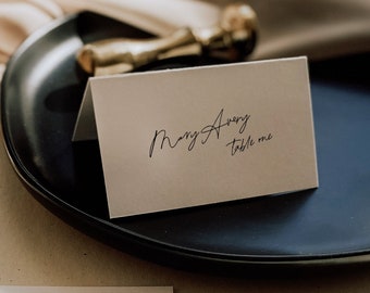 Può includere: Segnaposto bianchi con calligrafia nera per un ricevimento di nozze. Le carte recitano "Mary Avery table one". Le carte sono su un piatto nero e una superficie bianca. Il testo "SINCERELY by nicole" è visibile nella parte inferiore dell'immagine.