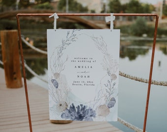 May include: A white wedding sign with a watercolor design of seashells and coral. The sign reads "Welcome to the wedding of Amelia and Noah, June 13, 20xx, Destin, Florida".