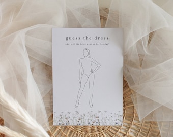 Può includere: Un biglietto bianco con il testo "guess the dress" e "what will the bride wear on her big day?"  Un disegno a linea di una donna con un vestito è sul biglietto. Il biglietto è su una superficie di vimini intrecciato con una piuma bianca.