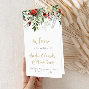 Puede incluir: Un programa de boda blanco con letras doradas. El programa presenta una ilustración de acuarela de vegetación, bayas rojas y flores blancas. El texto dice "Bienvenido a la boda de Amelia Edwards y Noah Davis Sábado 11 de noviembre de 20xx Golden, Colorado".