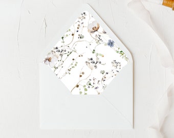 Puede incluir: Un sobre blanco con un patrón floral en la solapa. El patrón presenta delicadas flores y hojas azules y marrones sobre un fondo blanco.