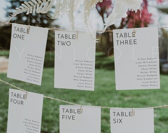 Può includere: Un set di sei carte bianche con testo nero, appese a una corda con mollette. Ogni carta ha un numero di tavolo e un elenco di nomi. Le carte sono etichettate "Tavolo Uno", "Tavolo Due", "Tavolo Tre", "Tavolo Quattro", "Tavolo Cinque" e "Tavolo Sei".